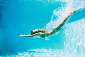 Young woman with long blonde hair diving into a swimming pool